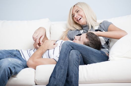 Laughing couple relaxing on couch, with man lying with his head in the woman's lap. Horizontal format.