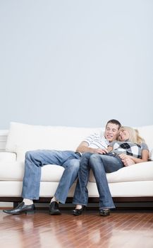 Full length view of affectionate couple laughing and relaxing together on white couch. Vertical format.