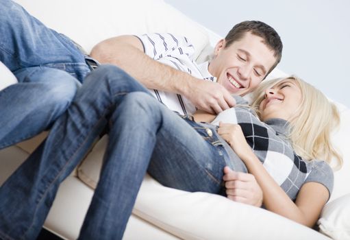 Cropped tilt view of affectionate couple laughing and relaxing together on white couch. Horizontal format.