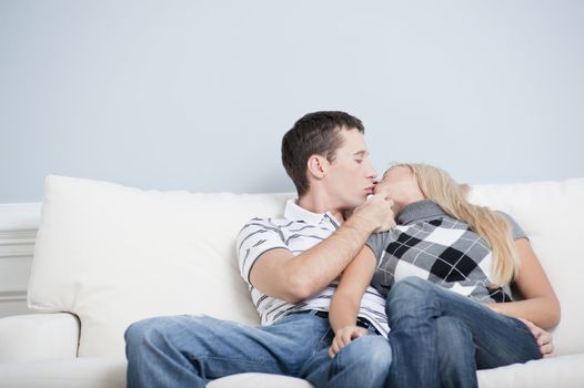 Cropped view of couple sitting on white couch and kissing. Horizontal format.