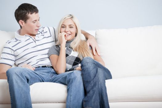 Cropped view of affectionate couple relaxing together on white couch, with woman smiling at the camera. Horizontal format.