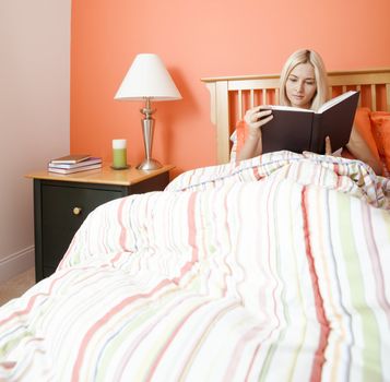 Blonde woman sitting in bed and reading a book. Square format.