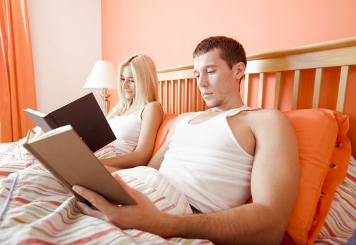 Man and woman reading side-by-side in bed. Horizontal format.