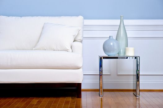 Cropped view of white couch and side table with vases, in a living room with a wood floor. Horizontal format.