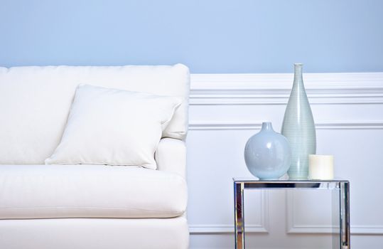 Cropped view of a living room, focusing on a white couch and side table with vases. Horizontal format.