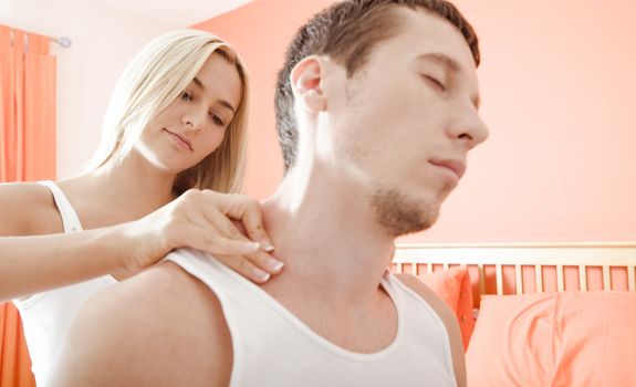 Man and woman sit on bed as woman massages man's shoulders. Horizontal format.
