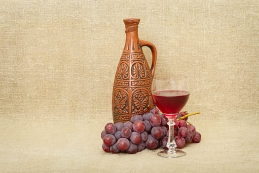 Still-life from a clay bottle, grapes and wine against a canvas