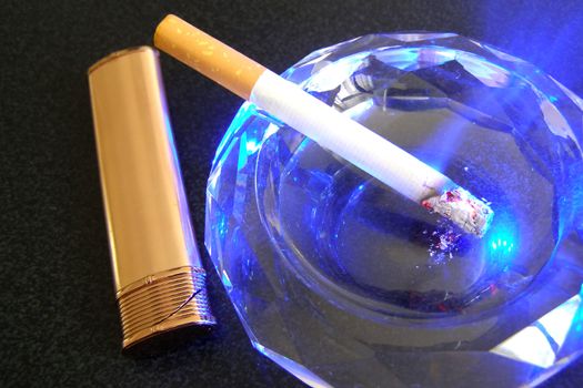 cigarette in ashtray and lighter on the black table    