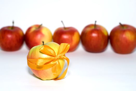 red apples behind a yellow apple with a gift bow