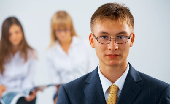 Portrait of young serious business man with two women on the background