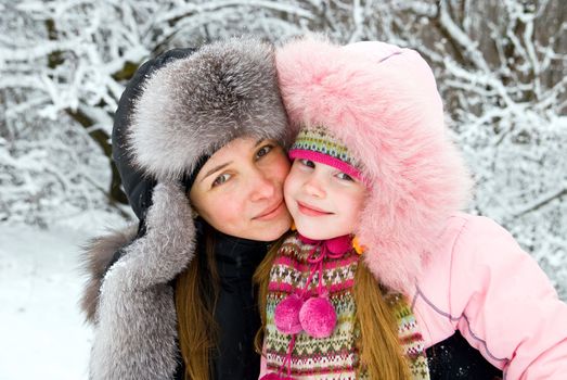 young mother and daugther in winter clothing hugging in a winter woods