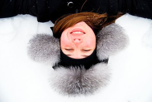 beautiful girl in fur hat lying in the snow upside down