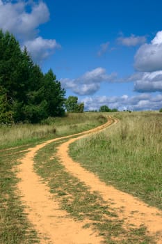 Sand track in the field under the dark blue sky with clouds
