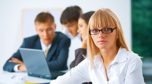 Portrait of young serious business woman with her working colleagues at the background