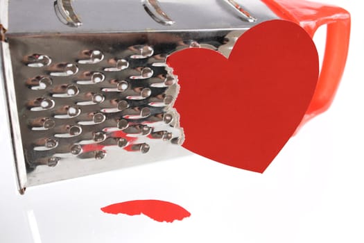The broken off red paper heart against a kitchen grater removed close up