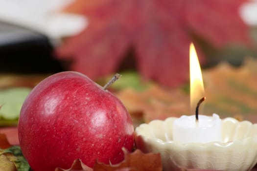 Burning candle with a red apple removed close up against autumn leaves