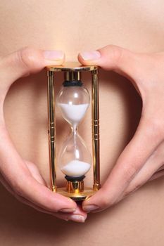 Sand-glass in female hands against a stomach removed close up