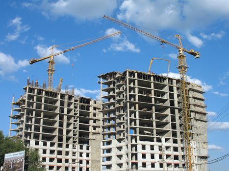 Two yellow tower cranes on a construction site on a background of the sky with clouds, (look similar images in my portfolio)