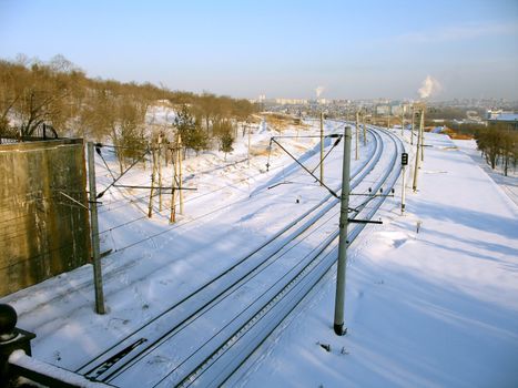Railroad tracks covered by a snow near a hill and a line of a contact network on a background of city, (look similar images in my portfolio)