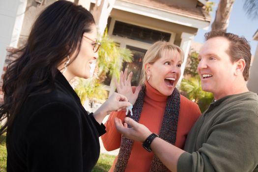 Hispanic Female Real Estate Agent Handing Over New House Keys to Excited Couple.