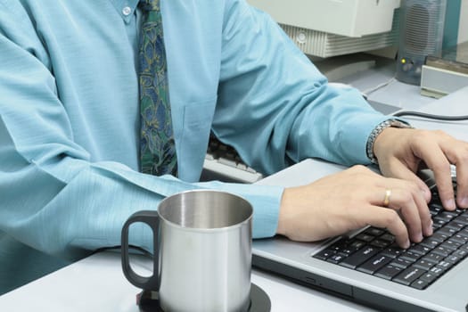 male executive  working on a laptop with tin cup on the side
