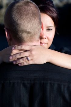 A pretty young woman hugs her husband or fionce.  Shallow depth of field with focus on the diamond engagement ring.
