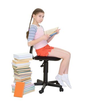 The schoolgirl learns lessons sitting near the big pile of books and textbooks