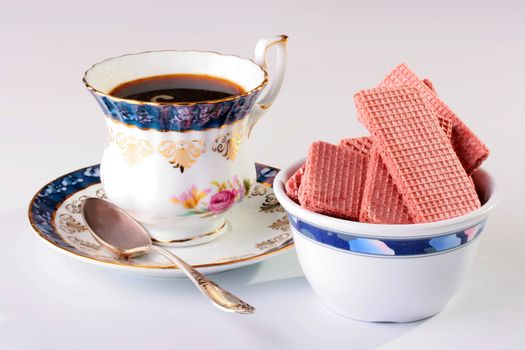 Cup of black coffee on a saucer with a spoon and wafers in ceramic ware.
