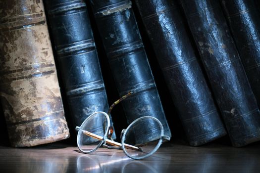 Vintage eyeglasses on dark background with row of old books