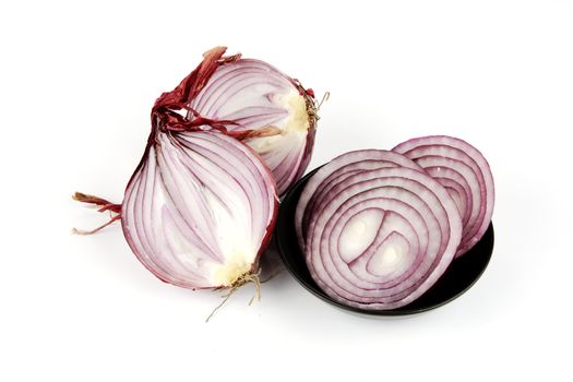 Raw red onion cut in half with slices in a small black dish on a reflective white background