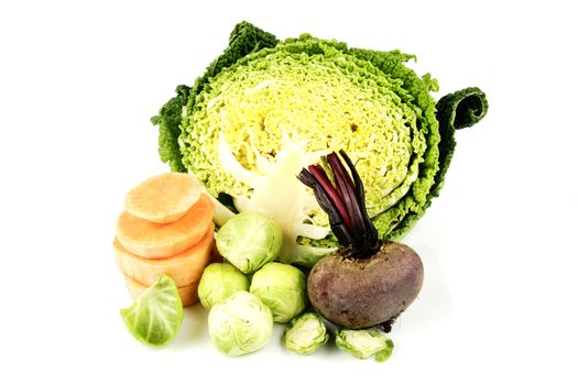 Half a raw green cabbage with raw beetroot, sprouts and slices of sweet potato on a reflective white background
