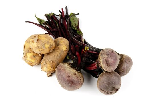 Bunch of raw red beetroot with a pile of small brown potatoes on a reflective white background