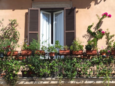A balcony with flowers and a window with brown shutters - typical Mediterranean architecture.