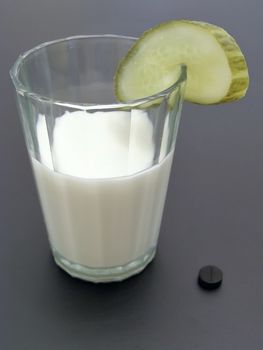 Glass of milk with piece of cucumber and 	activated carbon near it      