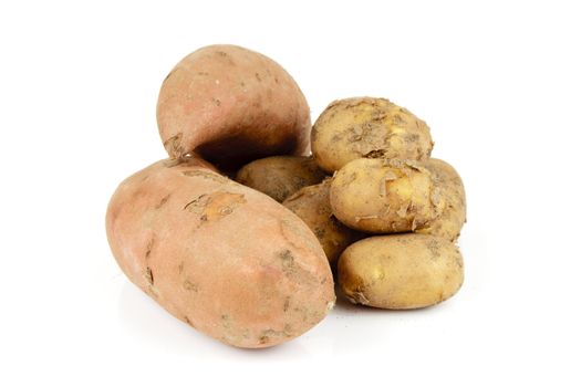 Small pile of brown unpeeled potatoes with two sweet potato on a reflective white background