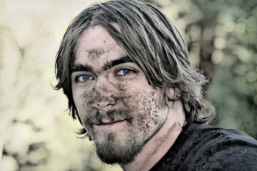 Handsome young man with blue eyes has his face covered with mud after negotiating a particularly muddy ATV trail.