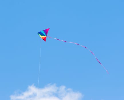 Child's toy kite in rainbow colors flying in a clear blue summer sky