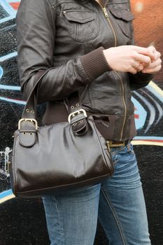 Woman dressed in leather clothes in front of a wall.