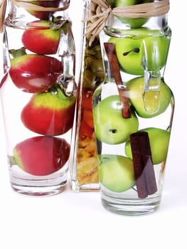 Glass jars filled with green apples and red pomegranates, on a white background.