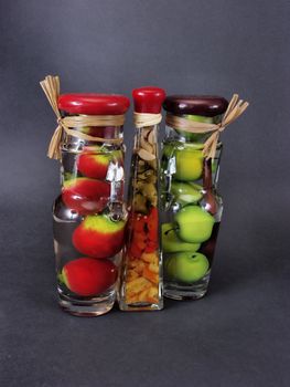 Glass jars filled with green apples, orange citrus, and red pomegranates, on a black background.