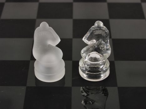 Knights of a different color face off on a clear glass etched chess board.