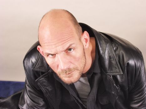 A middle aged balding man in a leather jacket doesn't look happy