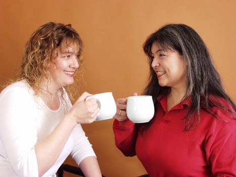 Two women drinking out of large coffee cups, facing toward eachother.