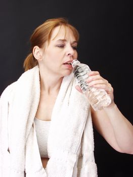 A woman with a white towel around her neck, prepares to quench her thirst with a drink from her water bottle