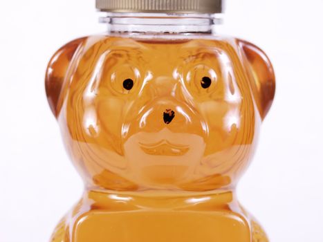 Close view of a bear shaped container full of golden honey. Over a white background.