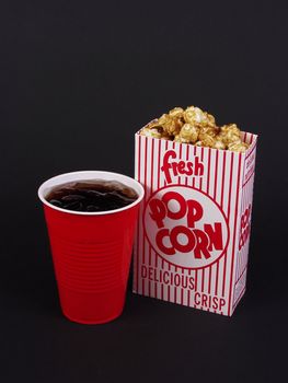 A box of caramel corn and a red cup of soda on a black background.