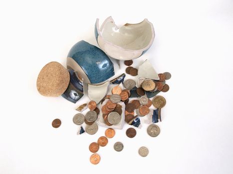 A change jar made of ceramic lays broken, coins spilled, ready to be counted up and spent. Over white.