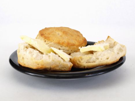 Biscuits with butter on a black plate over a white background with room for text.