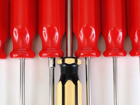 Red handled screwdrivers in a military line with a yellow handled screwdriver in command. Over white.