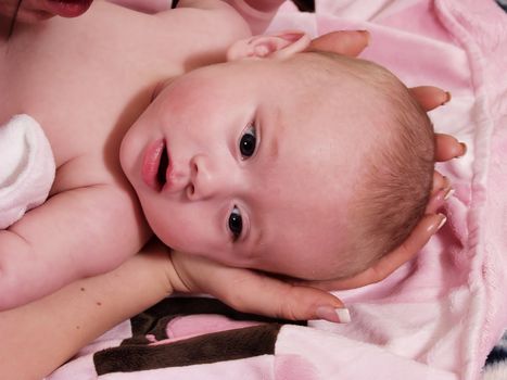 A mother cradles her young infant's head in her hands.  Surrounded in Pink tones.